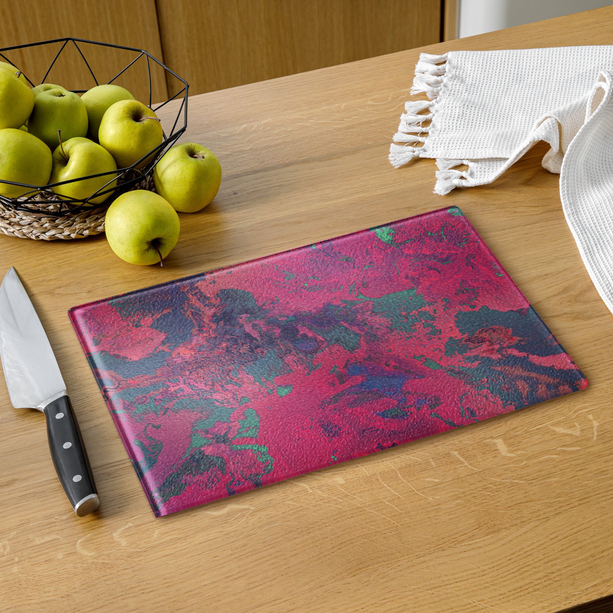 Colorful cutting board on a wooden table with apples and a knife.