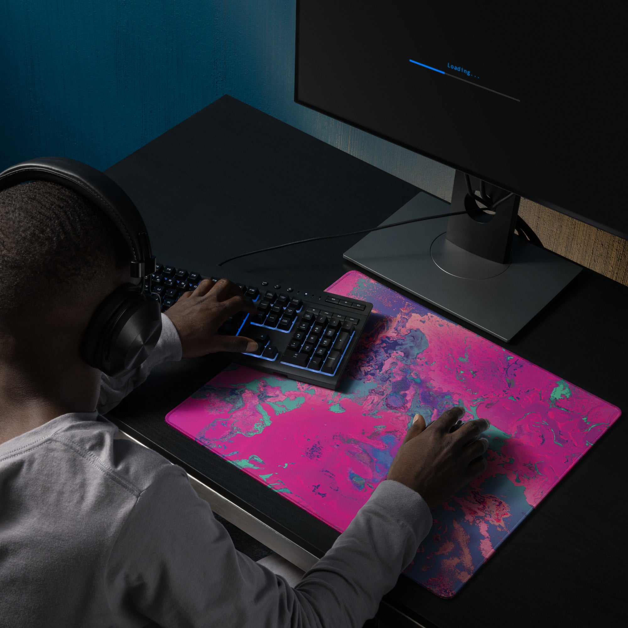 Person using a computer with a colorful mouse pad and headphones on a dark desk.