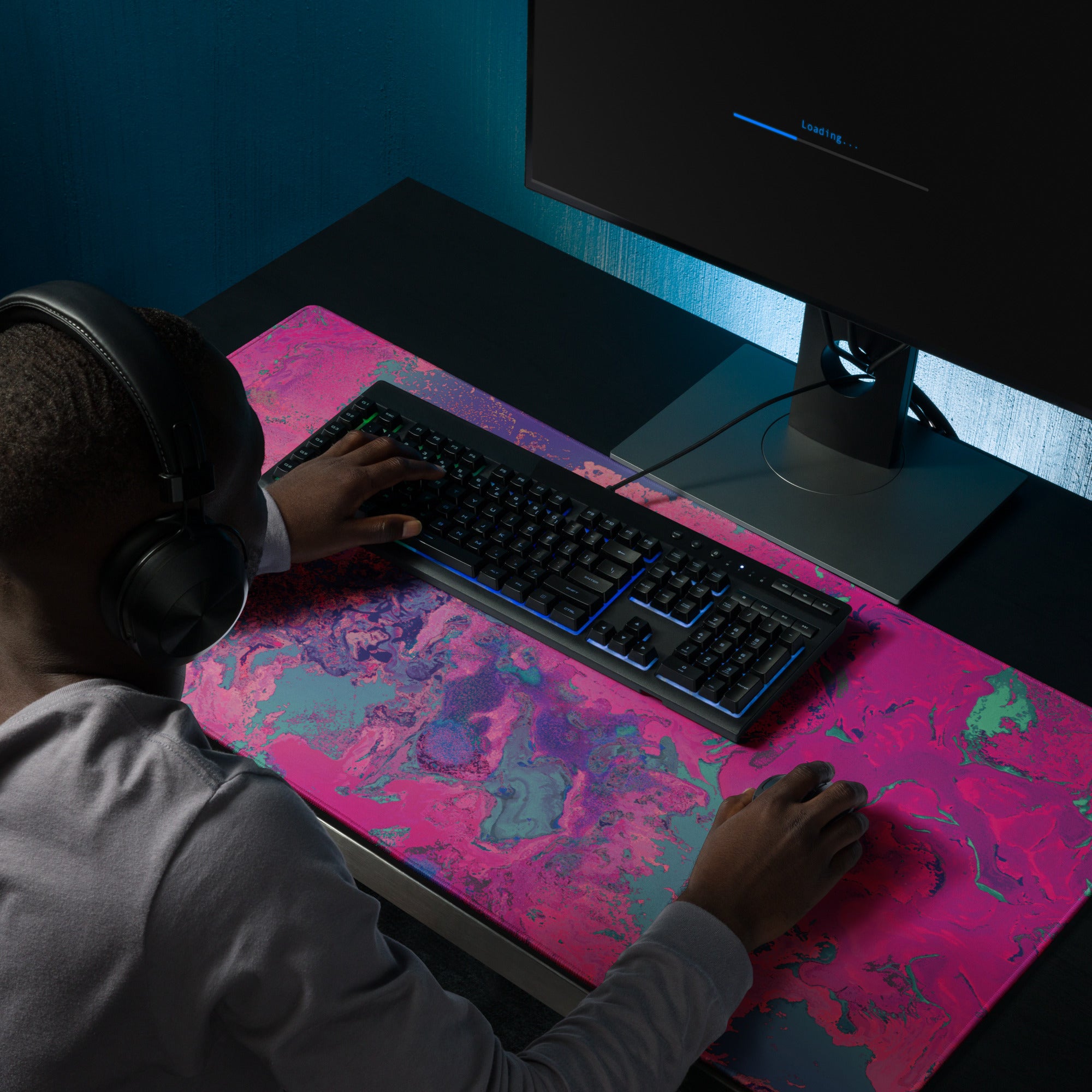 Person using a computer with a colorful mouse pad and headphones on a dark desk.