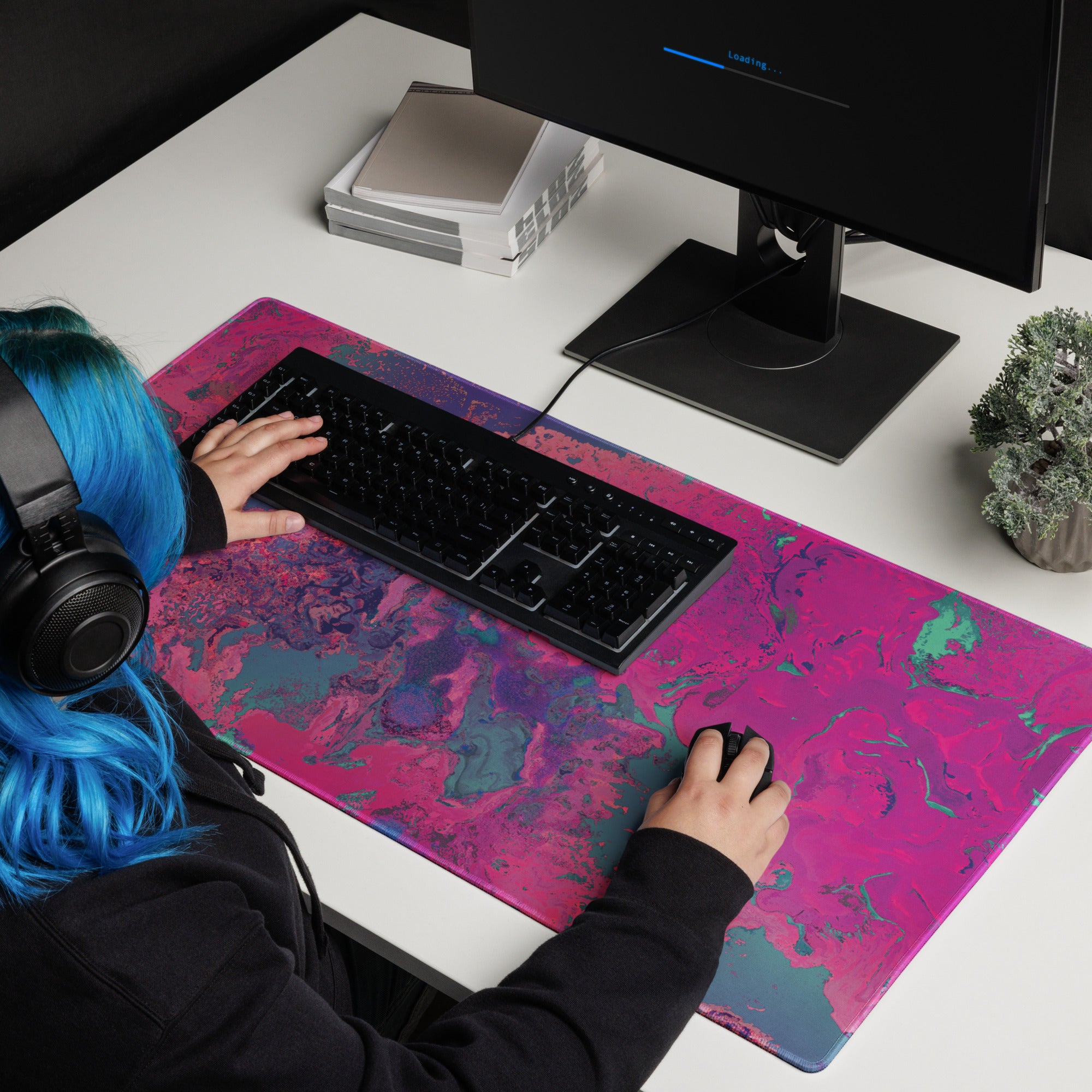 Person with blue hair using a computer on a desk with a colorful mouse pad.