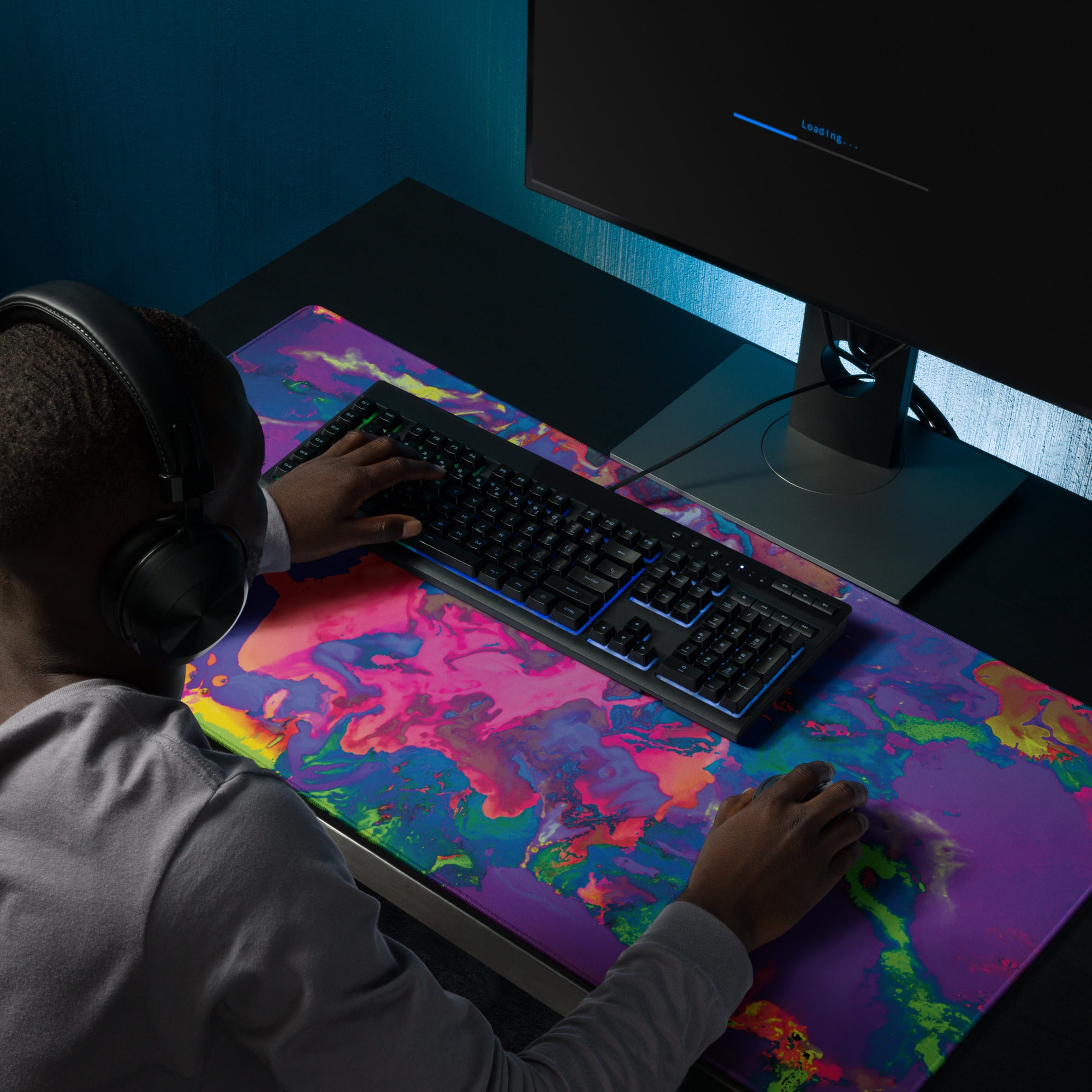 Person using a computer with a colorful desk pad and headphones in a dark room.