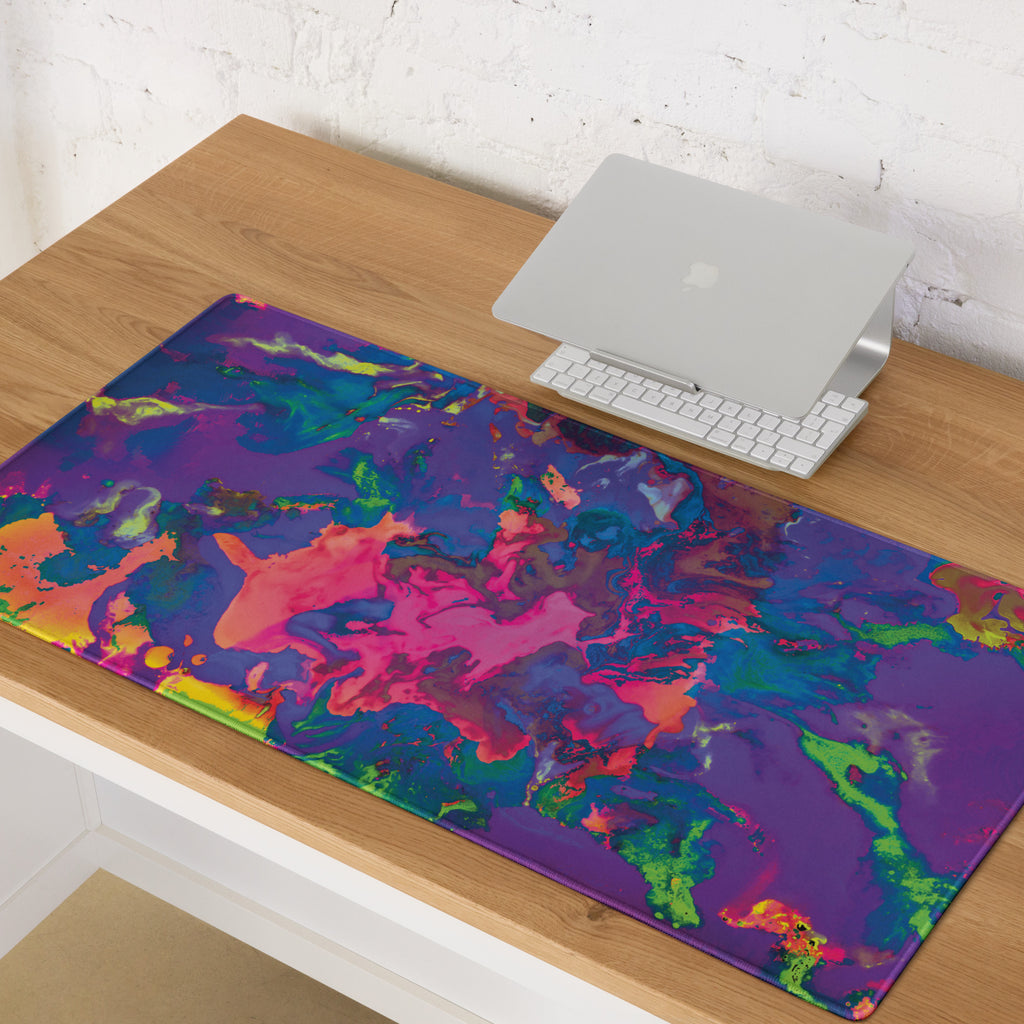 Colorful abstract gaming mouse pad on a wooden desk with a laptop and keyboard.