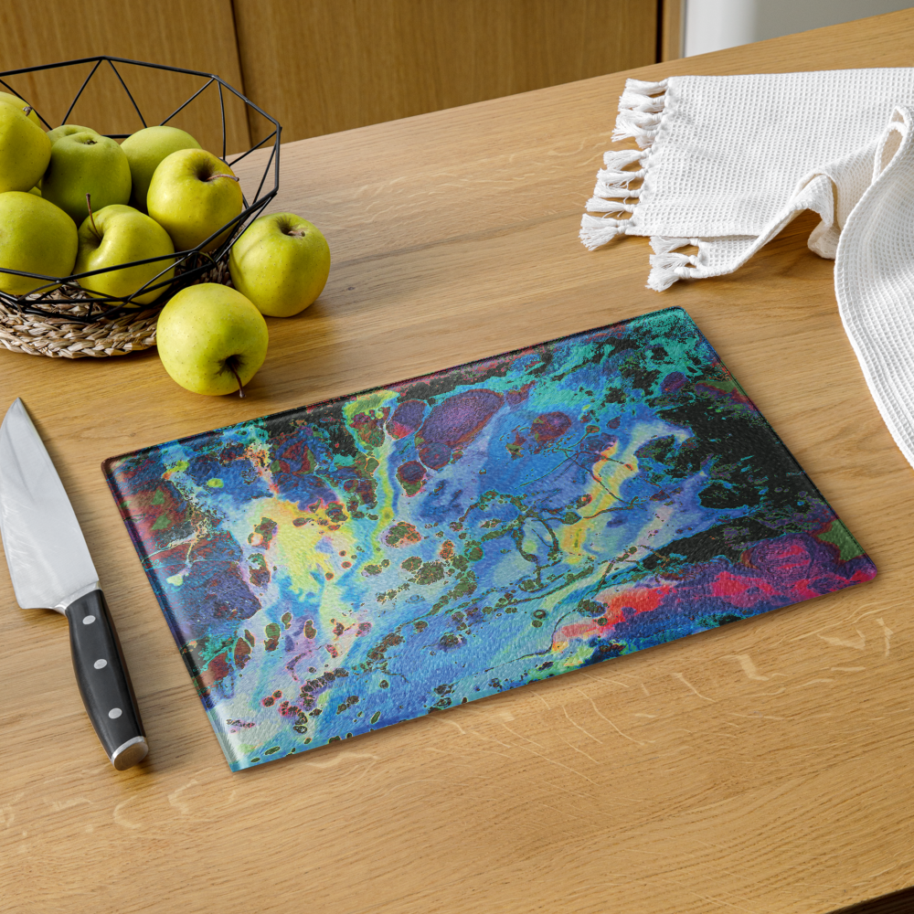 Colorful marbled blue glass cutting board on a wooden table with apples and a knife.