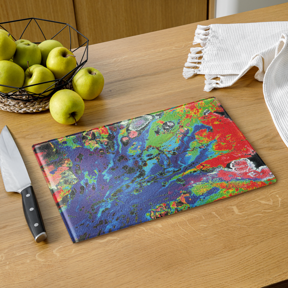 Colorful marbled glass cutting board on a wooden table with apples and a knife.