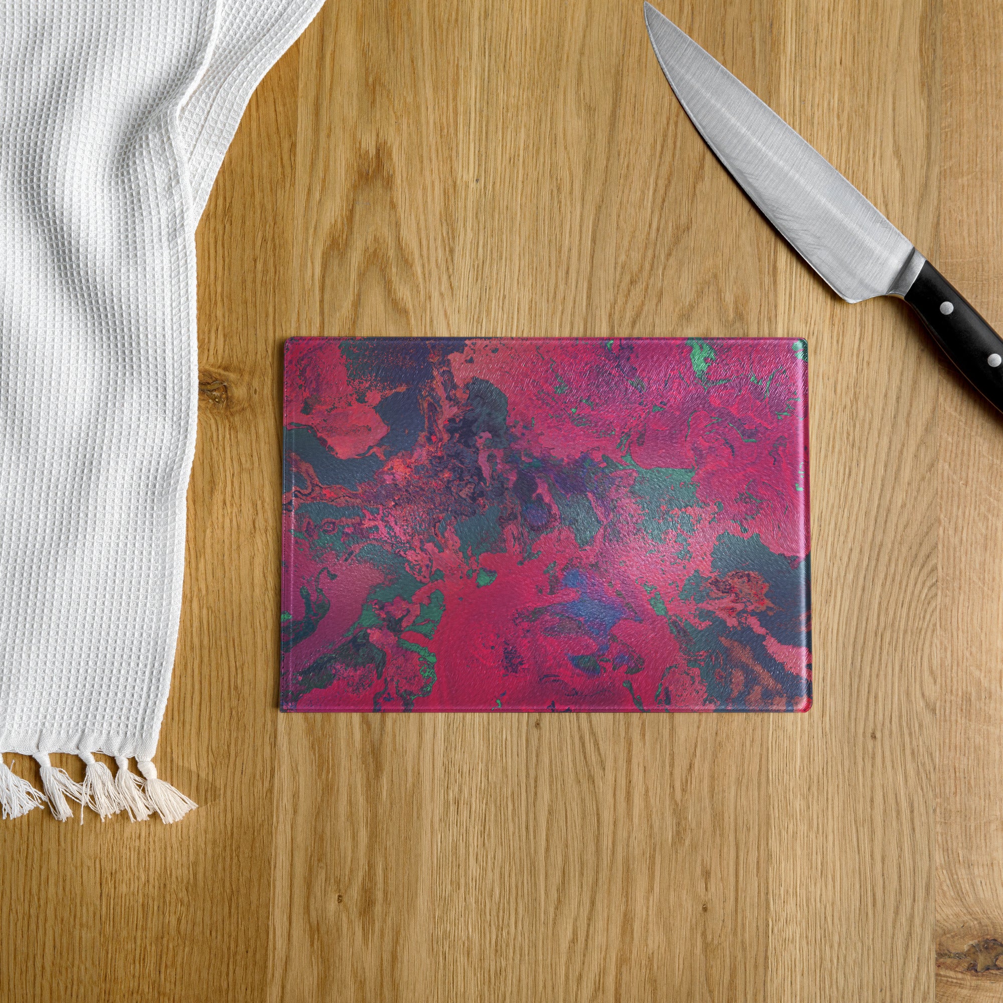 Colorful cutting board on a wooden surface with a knife and white towel.