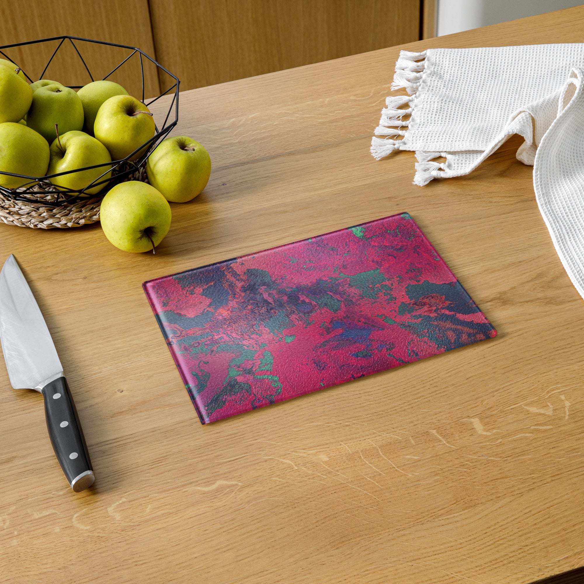 Pink and blue patterned cutting board on a wooden table with apples and a knife.