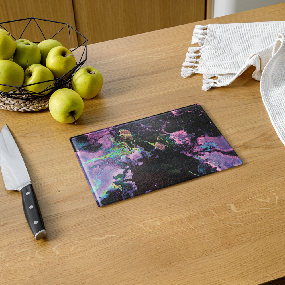 Glass cutting board with an abstract lavender design on a wooden table with apples and a knife.