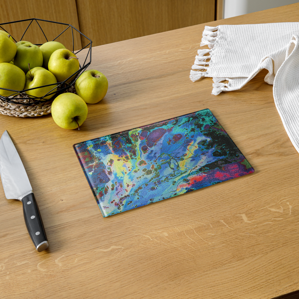 Colorful glass cutting board on a wooden table with apples and a knife.