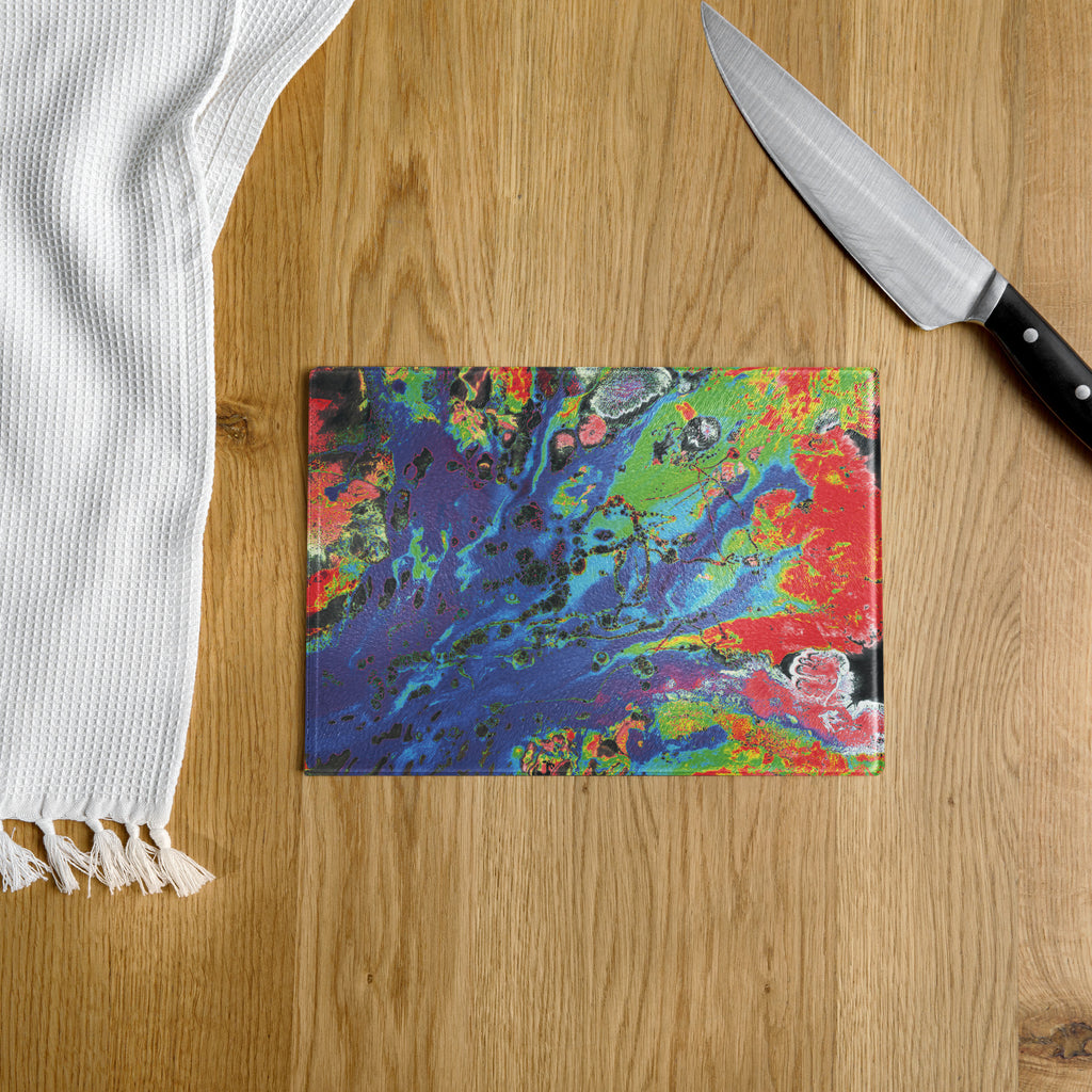 Colorful abstract-patterned cutting board on a wooden surface with a knife and white towel.