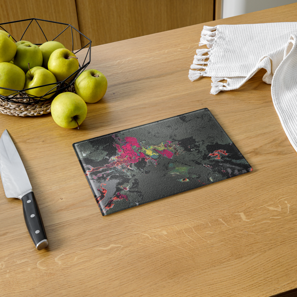 Glass cutting board with colorful design on a wooden table with apples and a knife.