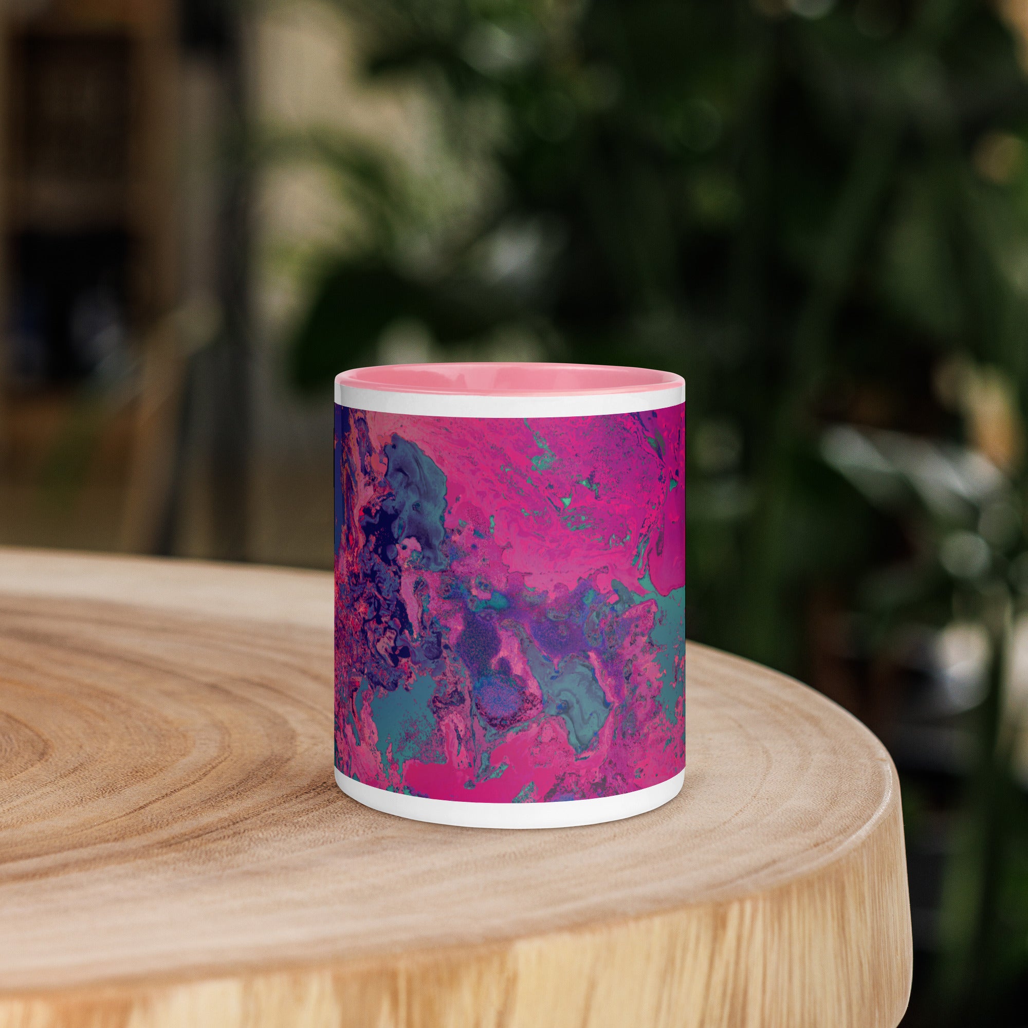 Pink and blue abstract-patterned mug on a wooden surface with a blurred green background