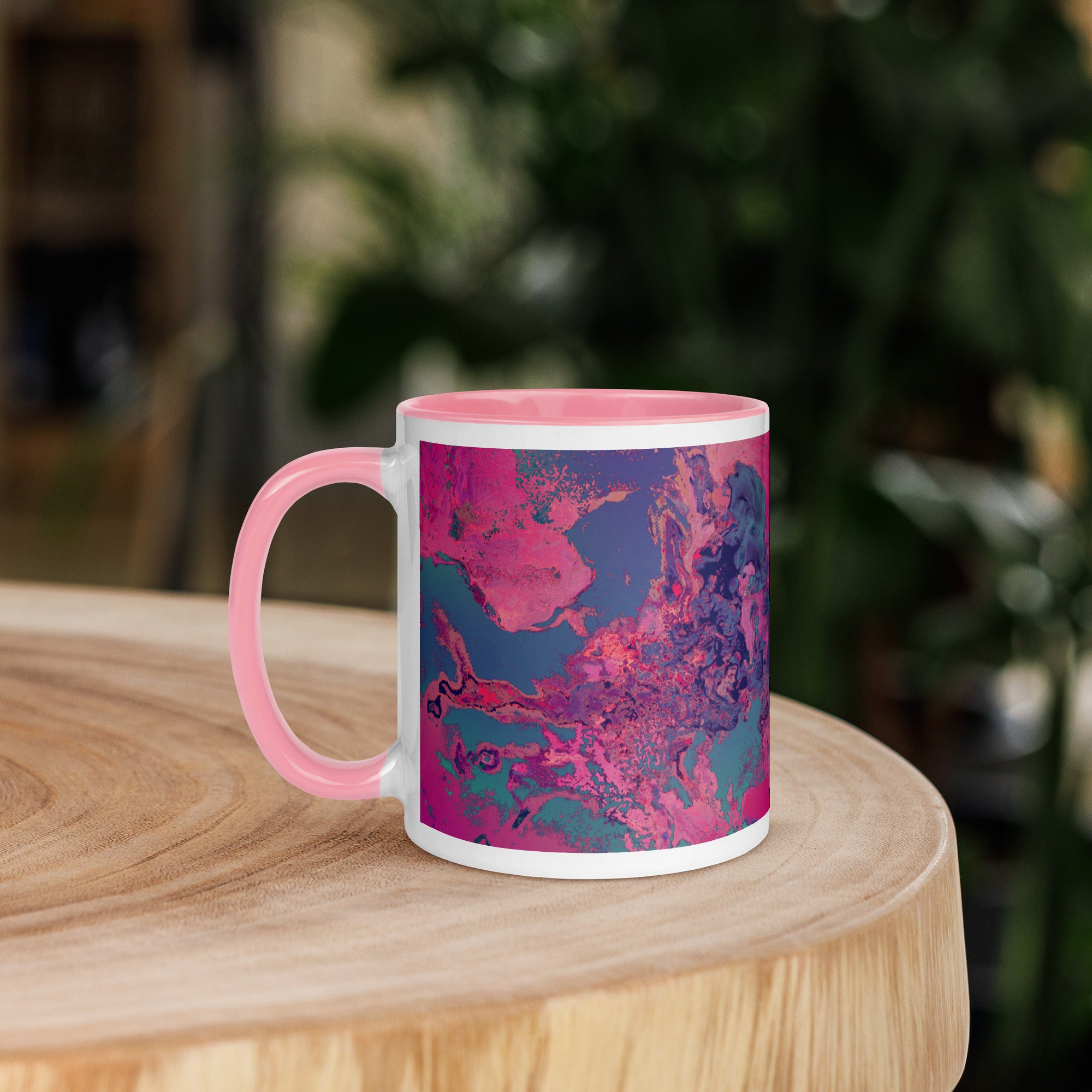 Mug with pink and blue abstract design on a wooden surface with a blurred green background